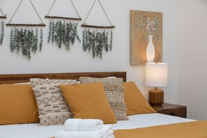 A neatly made bed with a white comforter and multiple pillows, a bedside lamp, and a wall-mounted plant arrangement. - Hip Old Town North Gem! Near Breweries and River! (Fort Collins)