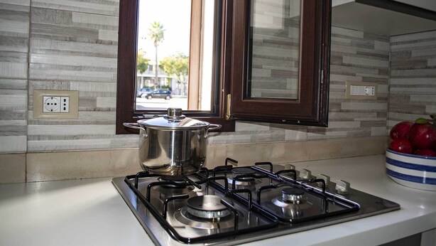 A kitchen with a gas stove, a pot on the stove, and a bowl of apples on the counter. - Casa Vacanze Mediterranea (Gagliano del Capo)