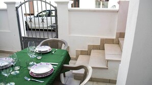 A dining table set with plates, glasses, and cutlery, surrounded by chairs, with a staircase and a gate in the background. - Casa Vacanze Mediterranea (Gagliano del Capo)