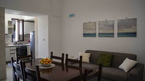 A modern kitchen with a stove, oven, and a dining area with a table set for two. There is a gray sofa with cushions and a small painting of a seascape on the wall. - Casa Vacanze Mediterranea (Gagliano del Capo)