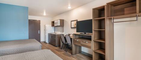 A modern bedroom with two beds, a desk, a TV, and built-in storage.