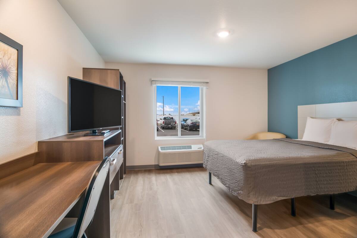 Une chambre d’hôtel moderne équipée d’un lit, d’un bureau, d’une télévision à écran plat et d’une fenêtre donnant sur les montagnes.