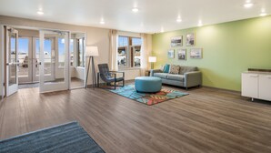 Ein modernes Hotelzimmer mit Holzboden, einem grauen Sofa, einem blauen Pouf und einem weißen Schrank.