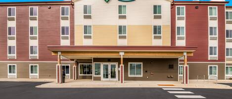 A multi-story hotel with a central entrance, a covered walkway, and a clear sky.