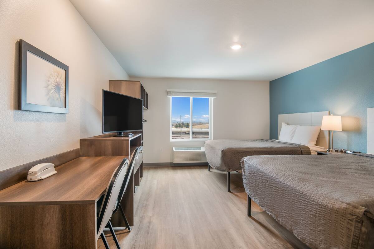 Une chambre d’hôtel équipée d’un bureau, de deux lits, d’une télévision et d’une fenêtre donnant sur un paysage agréable.