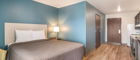 A bedroom with a bed, bedside table, lamp, and a door leading to a bathroom.