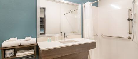 A bathroom with a wooden vanity, a sink, a mirror, a shower with a grab bar, and a towel rack.
