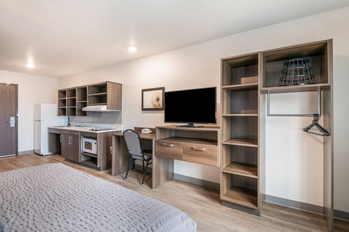 Une chambre moderne comprenant un lit, un bureau avec un ordinateur, une chaise et des étagères intégrées.