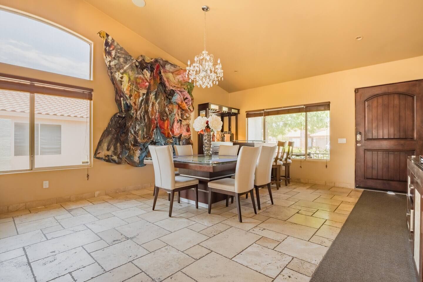 A dining area with a large abstract painting, a chandelier, and a view of the outside.