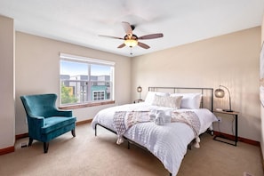 A bedroom with a bed, a chair, a ceiling fan, a window, and a nightstand. - Spectacular Townhome near Breweries and River District! (Fort Collins)
