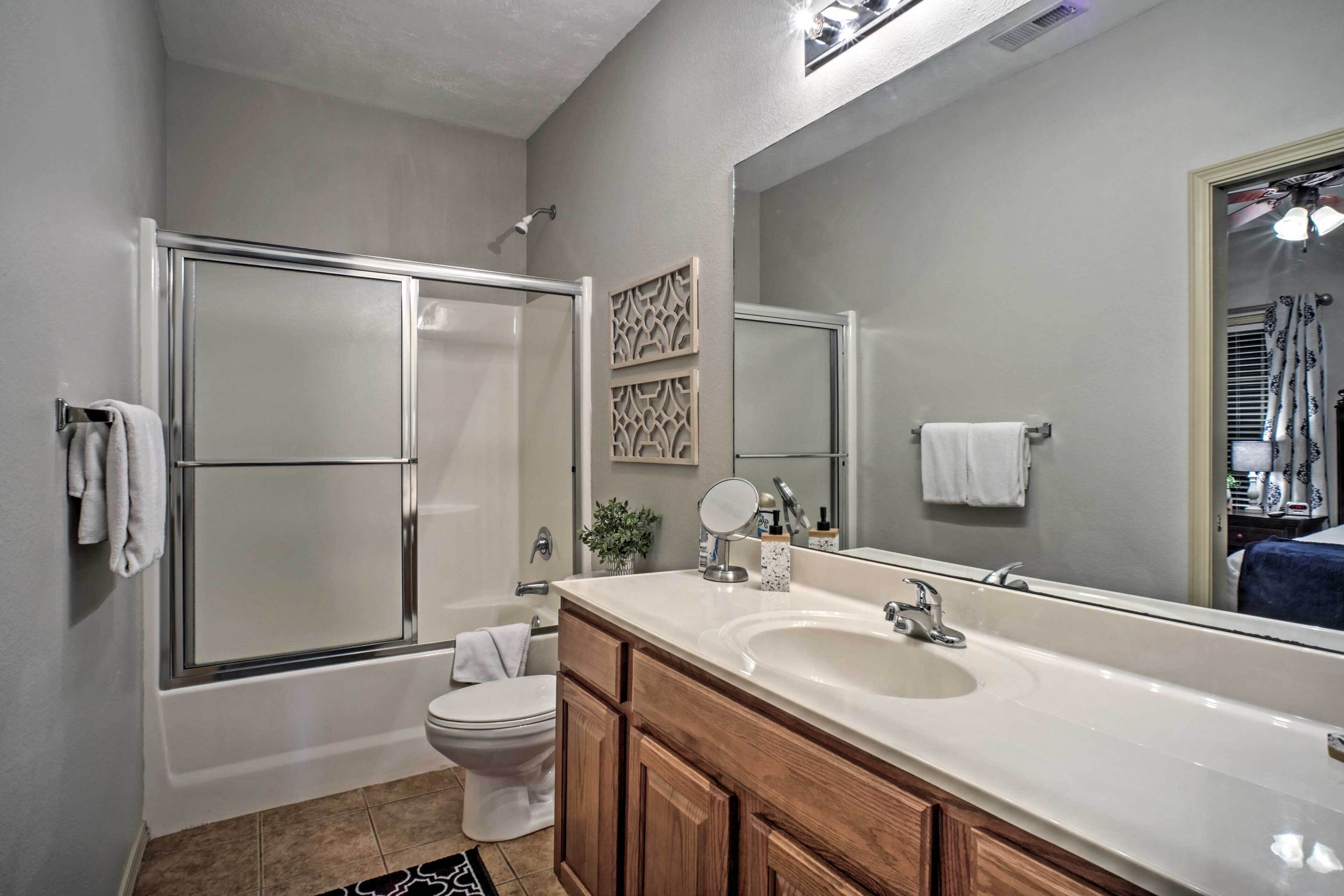 A bathroom with a shower, toilet, vanity, and large mirror.