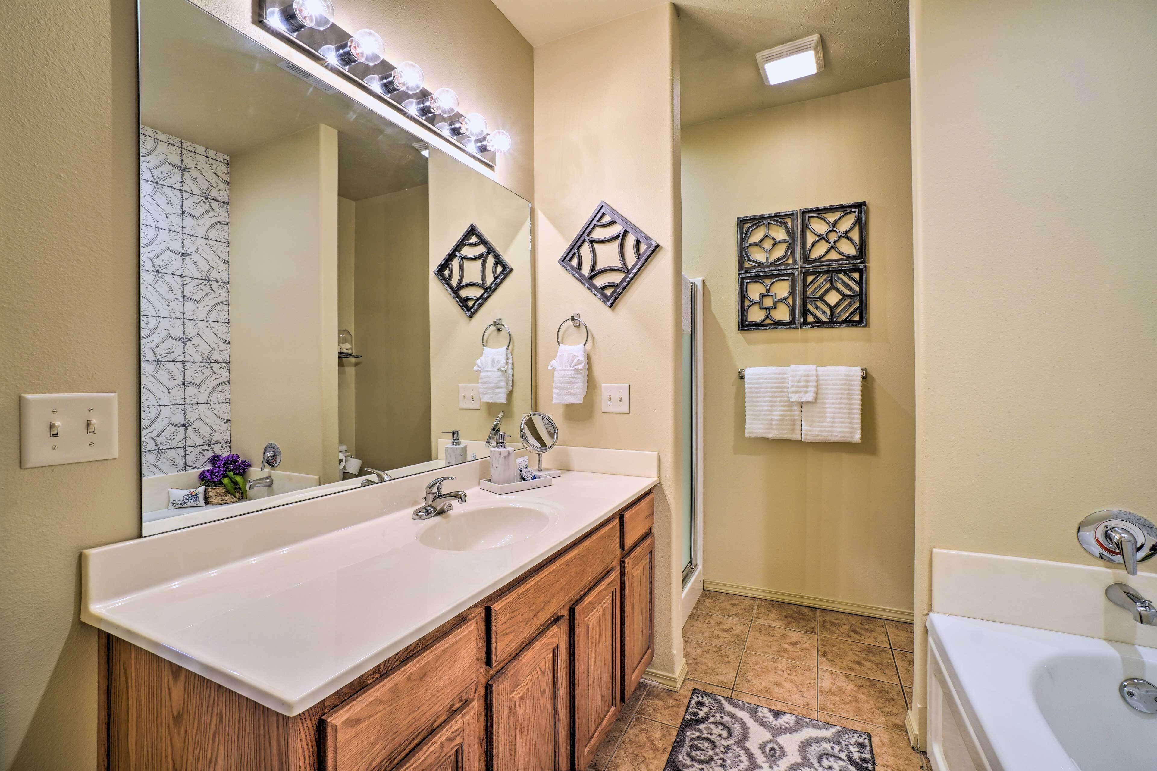 A bathroom with a large mirror, two sinks, wooden cabinets, and decorative wall art.