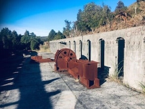 A large industrial machine with a wheel and metal structures, situated next to a concrete wall with arched openings. - Granity's Cosy Cottage (Granity)