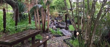 Un banco de madera en un área boscosa con un sendero de grava que lleva a una pila de troncos.