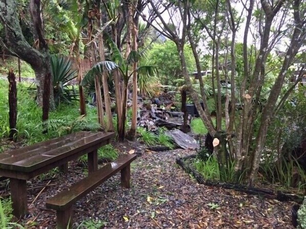 A wooden bench in a forested area with a gravel path leading to a pile of logs.