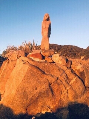 A large rock formation with a statue on top, surrounded by smaller rocks and sparse vegetation. - Granity's Cosy Cottage (Granity)