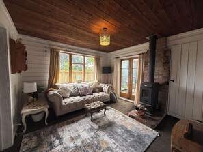 A cozy living room with a wooden ceiling, a sofa with cushions, a patterned rug, and a fireplace.