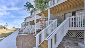 A multi-story residential building with white railings, a palm tree, and a concrete pathway. - Relaxing Harbor Island Condo: Walk to the Beach! (St. Helena Island)