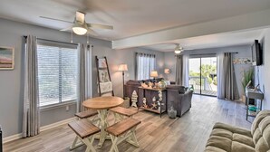 A spacious living room with a wooden dining table, a sofa, and a TV mounted on the wall. - Relaxing Harbor Island Condo: Walk to the Beach! (St. Helena Island)