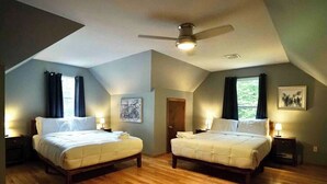 A room with two beds, wooden flooring, a ceiling fan, and artwork on the walls. - Lake Adjacent Home w/ Hot Tub, Game Room, Boats, Fenced Yard (East Stroudsburg)