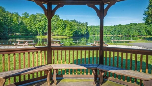 A wooden gazebo with benches overlooking a lake surrounded by trees. - Lake Adjacent Home w/ Hot Tub, Game Room, Boats, Fenced Yard (East Stroudsburg)