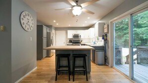 A modern kitchen with a central island, bar stools, and a ceiling fan. - Lake Adjacent Home w/ Hot Tub, Game Room, Boats, Fenced Yard (East Stroudsburg)