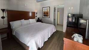 A hotel room with a large bed, a wooden headboard, a bedside table with a lamp, a refrigerator, and a TV. - Super 8 by Wyndham San Jose Airport (San Jose)