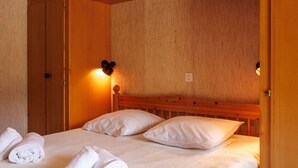 A single bed with white linens and pillows, a wooden headboard, a wall-mounted light fixture, and a small bedside table with a lamp. - Cosy apartment for 4 people with WIFI, TV and balcony (Basse-nendaz)