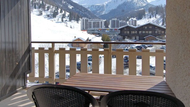 A balcony with a view of a snowy mountain landscape, a parking lot, and a building labeled "Raffels Switzerland." - Cosy apartment for 4 people with WIFI, TV and balcony (Basse-nendaz)
