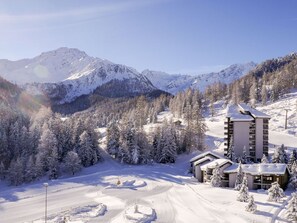 Une station de montagne enneigée, dotée d’une piste de ski, d’un chalet et offrant une vue sur les montagnes environnantes.