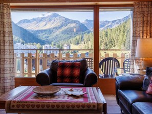 A balcony with a leather sofa and a table, overlooking a mountainous landscape with buildings in the background.