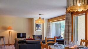 A living room with a sofa, dining table, chairs, a TV, a fireplace, and a large window. - Nice apartment for 8 guests with WIFI, TV and terrace (Basse-nendaz)