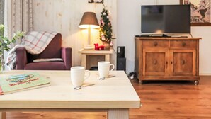 A cozy living room with a wooden coffee table, two white coffee mugs, a magazine, a television on a wooden cabinet, a Christmas tree, and a lamp. - Nice apartment for 4 people with WIFI, TV and balcony (Basse-nendaz)