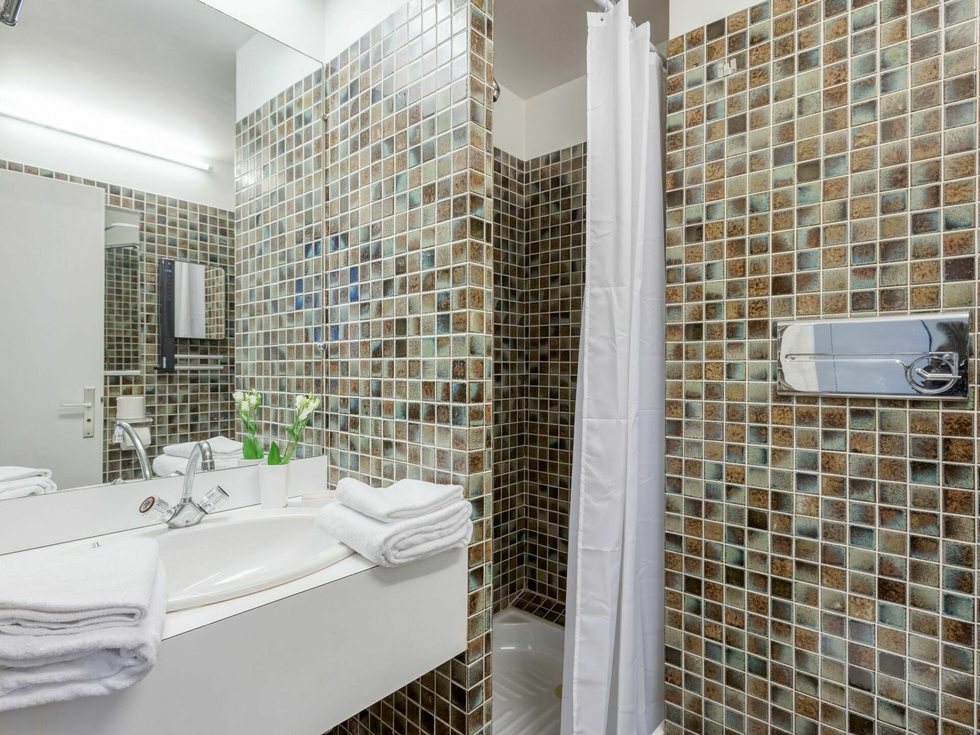 Une salle de bain avec un mur recouvert d’une mosaïque, un lavabo blanc et un rideau de douche.