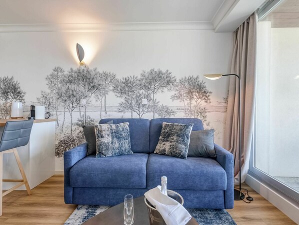 A modern living room with a blue sofa, a coffee table, and a wall mural.