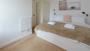 A bedroom with a bed, white walls, a door, and a painting on the wall. - Pebbles Apartment - Heart of Town (North Berwick)