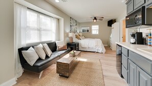 Un espacio habitable compacto con sofá, cama, zona de cocina y ventilador de techo.