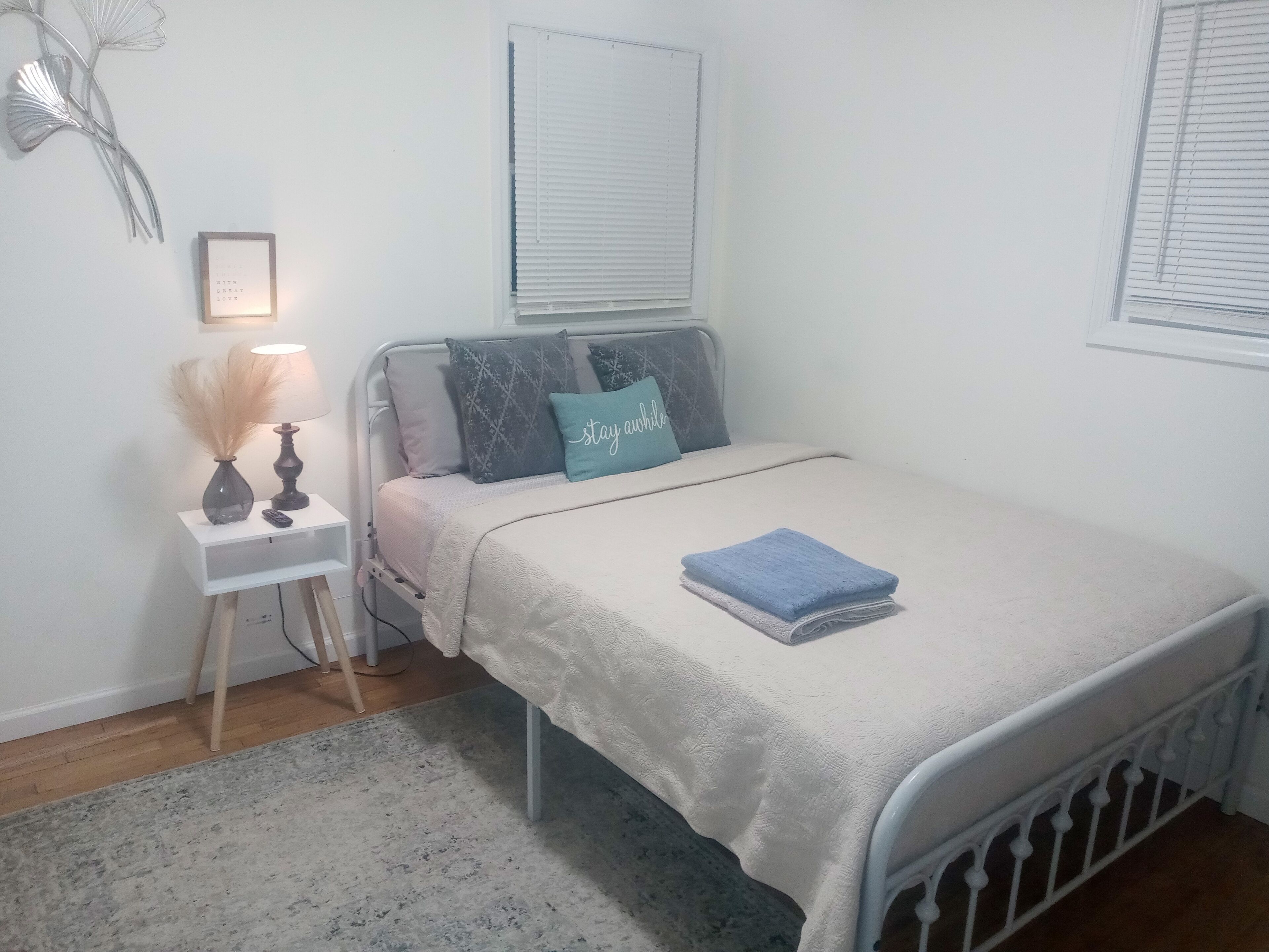 Une chambre à coucher bien rangée, avec un lit, une table de chevet, une lampe et des œuvres d’art décoratives au mur.
