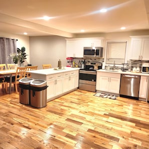 A modern kitchen with wooden flooring, stainless steel appliances, and white cabinetry.