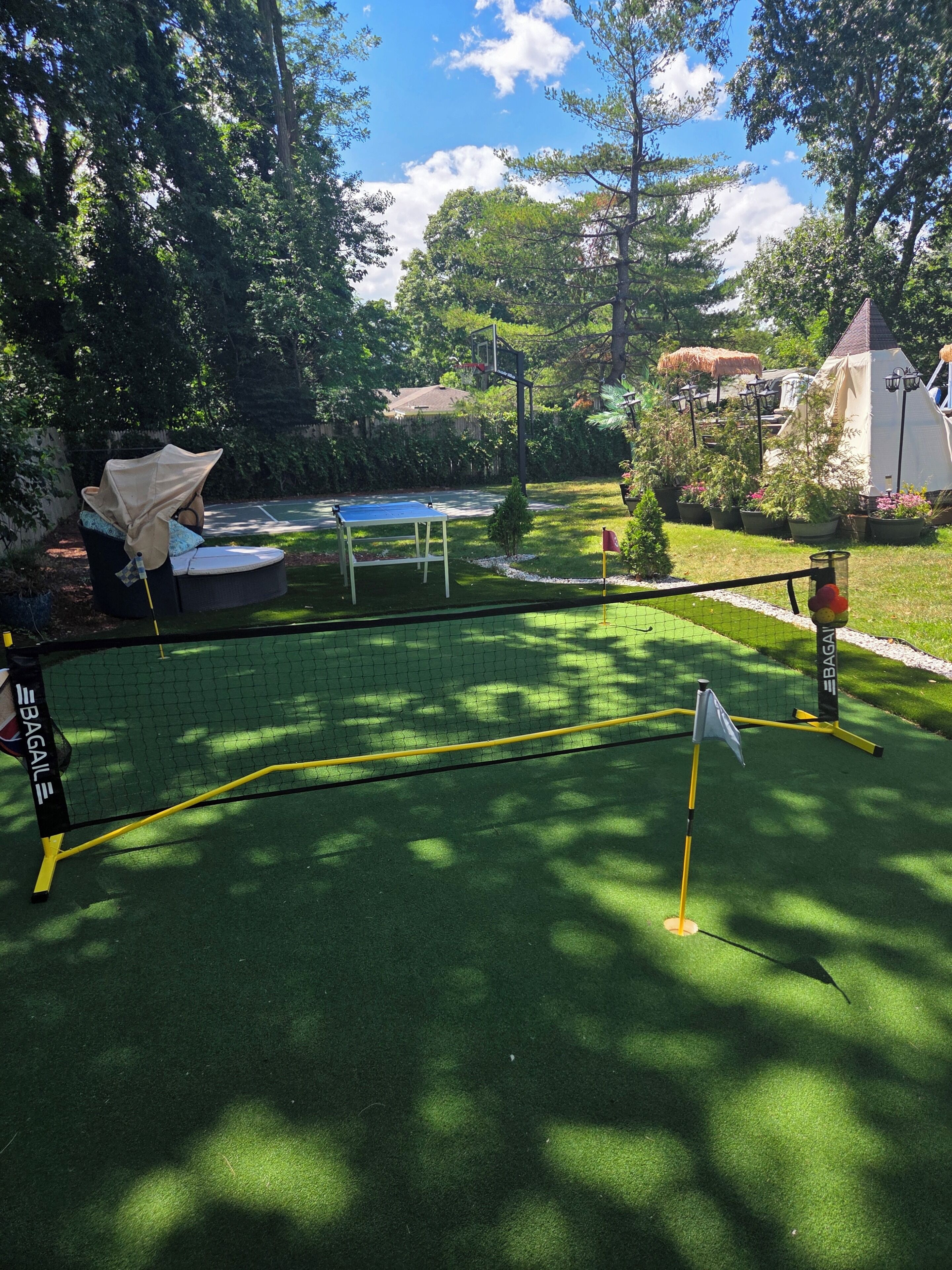 A green artificial turf area with a netted enclosure, a small flag, and a Bagaill brand table tennis table.