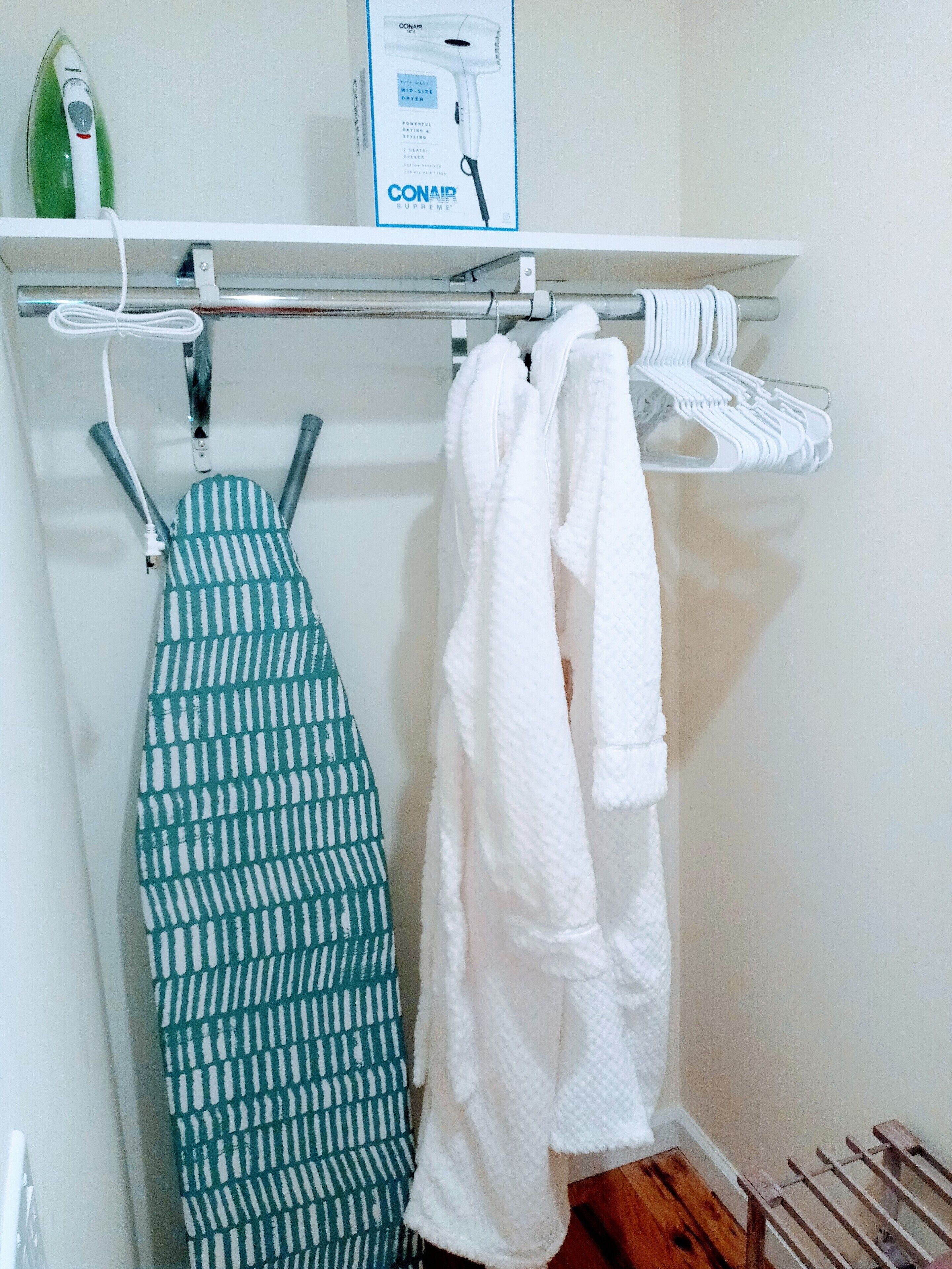 Een badkamer met een handdoekhouder waarop een witte handdoek en een groene handdoek liggen. Boven de houder staat een haardroger op de plank.