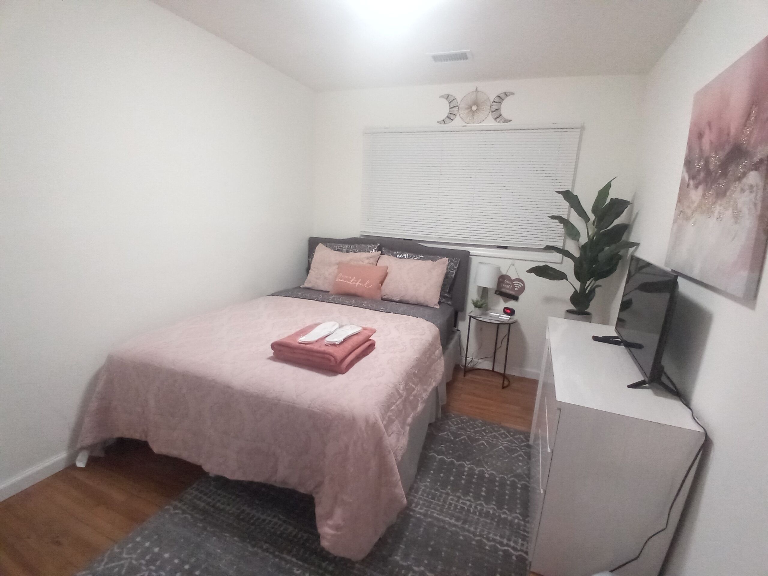 A bedroom with a bed, bedside table, lamp, and a plant.