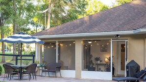 A covered patio area with a table and chairs, a lounge chair, and a grill. - 2 Acre FL Oasis with Game Room; Cozy+Quiet - Equestrian and Nature enthusiasts. (Ocala)