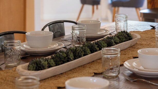 A dining table set with white bowls, plates, and glasses, with a wooden tray and succulents in the center. - 2 Acre FL Oasis with Game Room; Cozy+Quiet - Equestrian and Nature enthusiasts. (Ocala)