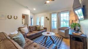 A living room with a brown leather sofa, a round coffee table, and a chair. There is a ceiling fan, a window with curtains, and a lamp on a side table. - 2 Acre FL Oasis with Game Room; Cozy+Quiet - Equestrian and Nature enthusiasts. (Ocala)