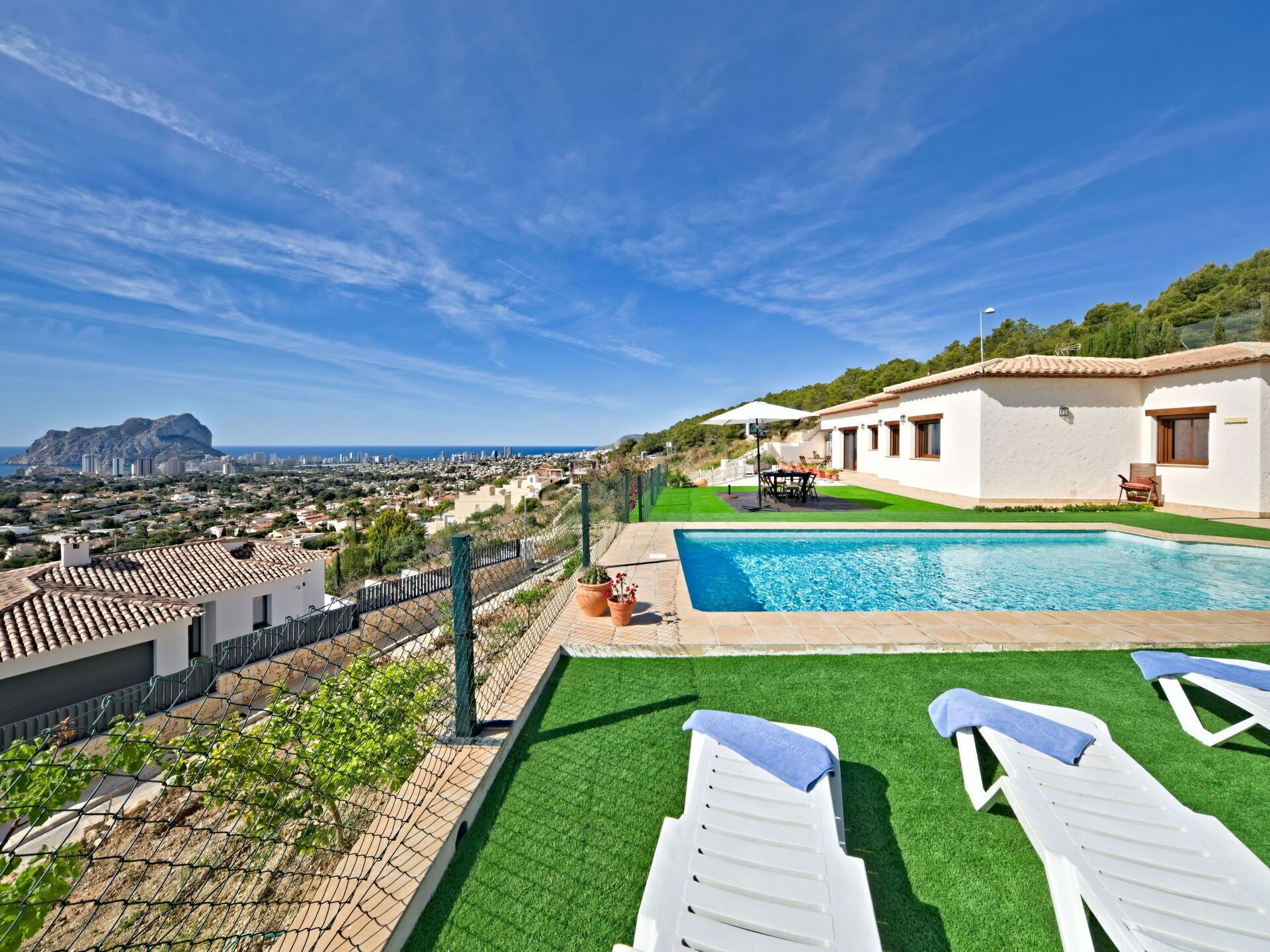 Une piscine sur le toit, agrémentée de gazon synthétique et de chaises longues, offrant une vue sur le paysage urbain et sur une montagne au loin.