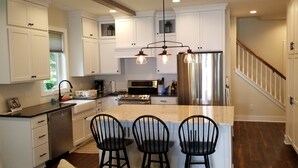 Una cocina moderna con armarios blancos, un refrigerador de acero inoxidable, horno empotrado e isla central con taburetes de bar.