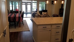Una cocina con armarios blancos, encimera de mármol y comedor con mesa para dos.