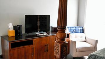 A bedroom with a wooden four-poster bed, a television on a wooden cabinet, and a chair with a blue and white blanket.