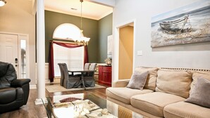 Olohuoneessa on lasinen sohvapöytä, beigenvärinen sohva ja seinällä oleva maalaus, jossa on kuvattuna vene.